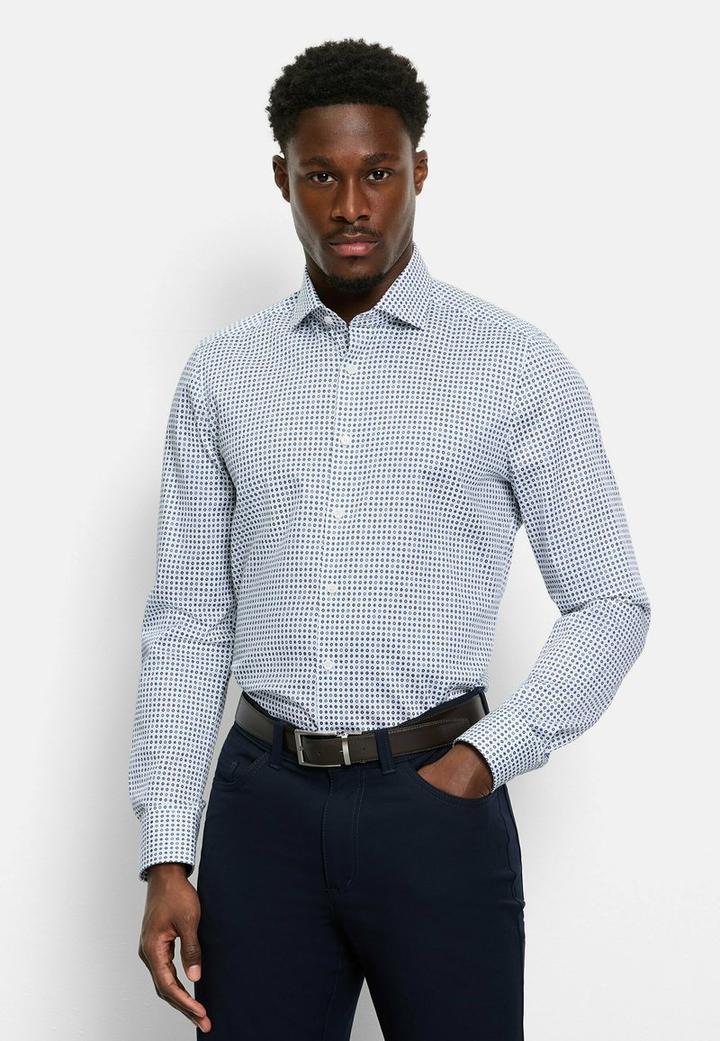 Weißes Langarmhemd mit blauem, kreisförmigem Muster, Button-Down-Kragen und schmaler Passform, kombiniert mit marineblauen Hosen und einem braunen Gürtel.