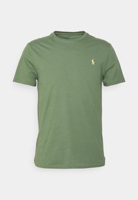 Vihreä puuvillainen T-paita, jossa on pyöreä pääntie ja lyhyet hihat. Vasemmassa rinnassa on pieni kultainen logo. Yksinkertainen malli.