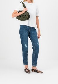 Top corto bianco a maniche corte, jeans blu strappati, ballerine con stampa leopardata nera e marrone, e una borsa a spalla verde oliva con una cerniera dorata.