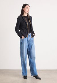 Schwarze Jacke mit einem Kragen aus Leopardenmuster, kombiniert mit hellblauen weiter geschnittenen Jeans und schwarzen spitzen Absätzen. Weicher Stoff, taillierter Schnitt.