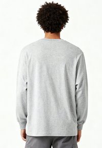 Persona con capelli ricci che indossa una maglia a maniche lunghe grigio chiaro tinta unita e pantaloni cargo grigi, vista di schiena su uno sfondo bianco.