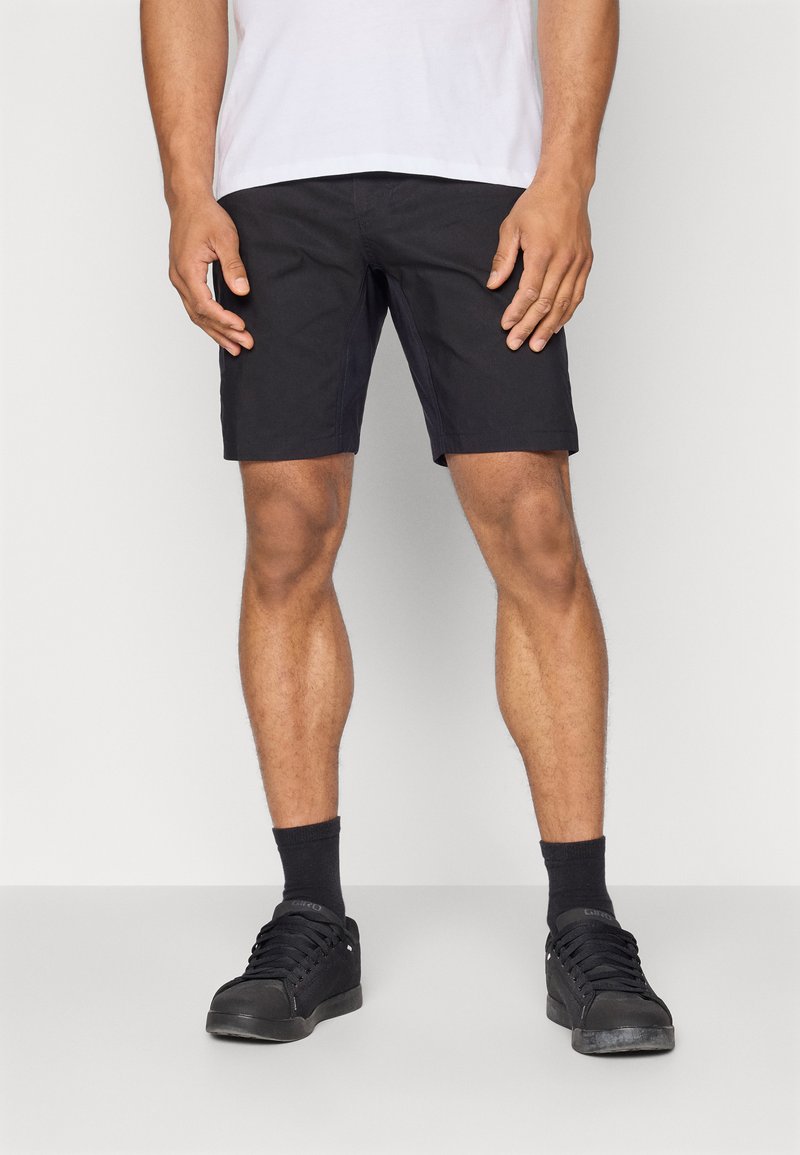 Schwarze Shorts aus leichtem Material mit geradem Schnitt. Kombiniert mit schwarzen Sneakers und Socken, vor einem neutralen Hintergrund.