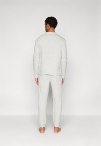 Top y pantalones de manga larga en gris claro, hechos de una tela suave. El top tiene un cuello redondeado, mientras que los pantalones cuentan con puños elásticos en los tobillos.