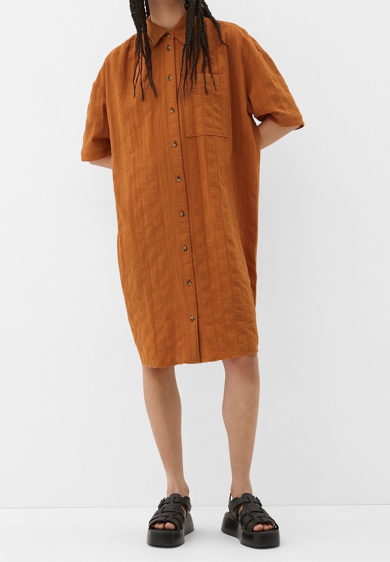 Personne portant une robe ample orange brûlé mi-longue boutonnée avec des manches courtes et des sandales plateformes noires.