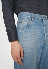 Denimjeans med en ljusblå tvätt, rak passform och subtila slitningar. Har en logotagg på främre fickan och knappstängning.