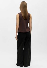 Haut sans manches marron associé à un pantalon large noir. Le haut présente une coupe décontractée, une texture lisse et un ourlet légèrement arrondi.