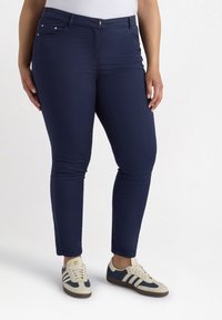 Marineblauwe fitted broek van een gladde, rekbare stof, met voorkeuringen met metalen accenten en een knoopsluiting aan de taille.