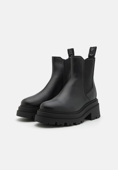Botas Chelsea de cuero negro con suela de plataforma gruesa, paneles laterales elásticos y lengüetas para facilitar el calzado. Diseño minimalista.