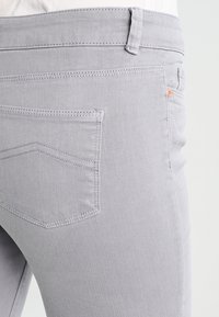 Lichtgrijze denim jeans met een standaard achterzakontwerp, opvallende stiksels en een kleine koperen accent nabij de tailleband.