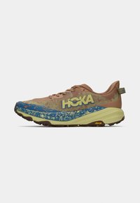 Tênis de corrida com um cabedal texturizado em marrom, salpicos azuis e verdes, e uma sola espessa e almofadada. Apresenta o logótipo "HOKA" na lateral.