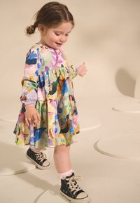 Kleurrijke gelaagde jurk met bloemenpatroon, lange mouwen en elastische manchetten. Gecombineerd met zwarte hoge sneakers en kanten sokken.