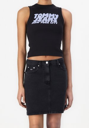 Zwart geribd mouwloos croptopje met witte tekst "TOMMY JEANS NEW YORK CITY", gecombineerd met een zwarte spijkerrok met voorzakken.