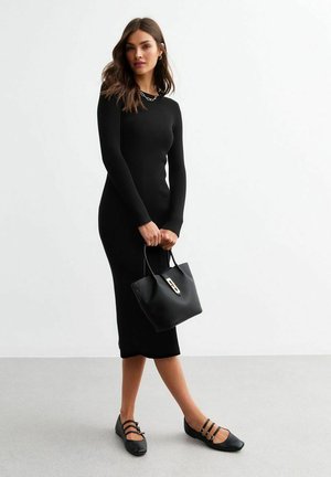 Abito midi nero a costine con maniche lunghe, abbinato a una borsa nera strutturata con chiusura dorata e scarpe nere piatte con dettagli a fascia.