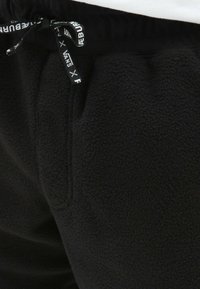 Sorte fleece sweatpants med snøre i taljen, prydet med sorte og hvide mærkeelementer og sidelommer. Blød tekstur.