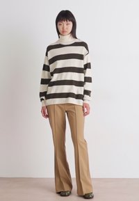 Stripet turtleneck genser i krem og mørkegrønn, laget av strikket stoff. Kombinert med brune bellbottom bukser og grønne sko. Enkelt, avslappet snitt.