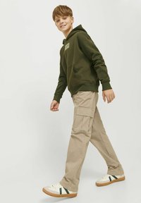 Kaki cargobyxor i kombination med en mörkgrön hoodie med framficka och logotypapplikation, kompletterat med beige sneakers med gröna detaljer.