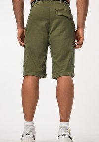 Shorts cargo verts olive avec ourlets roulés, fabriqués en matériau doux. Comprend des poches latérales et une taille noire avec un logo.