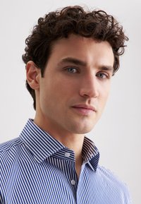 Camicia a righe blu e bianche con colletto button-down, caratterizzata da una texture liscia e righe uniformi. Il colletto presenta dettagli a contrasto.