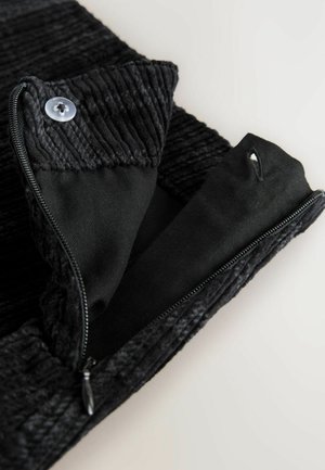Svart zippered plagg med en texturerad ribbad krage, som har en mjuk inre foder och en platt knappdetalj längst upp.