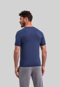 T-shirt blu navy a maniche corte realizzato in un tessuto liscio e aderente. Collo rotondo con orlo uniforme. Modello in piedi, che indossa pantaloni della tuta grigi.