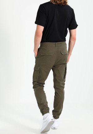 Khaki cargo tepláky s elastickými manžetami, několika bočními kapsami a hladkým texturovaným materiálem. Spárováno s černým tričkem s krátkým rukávem.