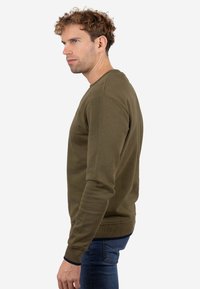 Sudadera verde oliva con cuello redondo, mangas largas, puños y cintura acanalados. Tejido suave con textura lisa. Sin logos ni patrones visibles.