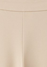 Gros plan d'un tissu beige avec une couture verticale et une couture horizontale courbée près du haut, montrant la texture et les détails des coutures.