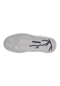 Semelle de sneaker blanche avec un motif de grip texturé, comportant un emblème circulaire et un détail de signature noire. Matériau en caoutchouc lisse.