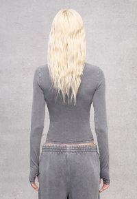 Maglietta grigia a maniche lunghe con un design aderente, texture morbida e dettagli di cucitura. Abbinata a pantaloni grigi con vita elastica coordinati.