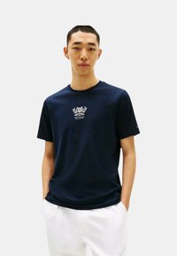 T-shirt in cotone blu scuro con stampa centrale bianca, scollo rotondo e maniche corte, abbinato a pantaloni bianchi.