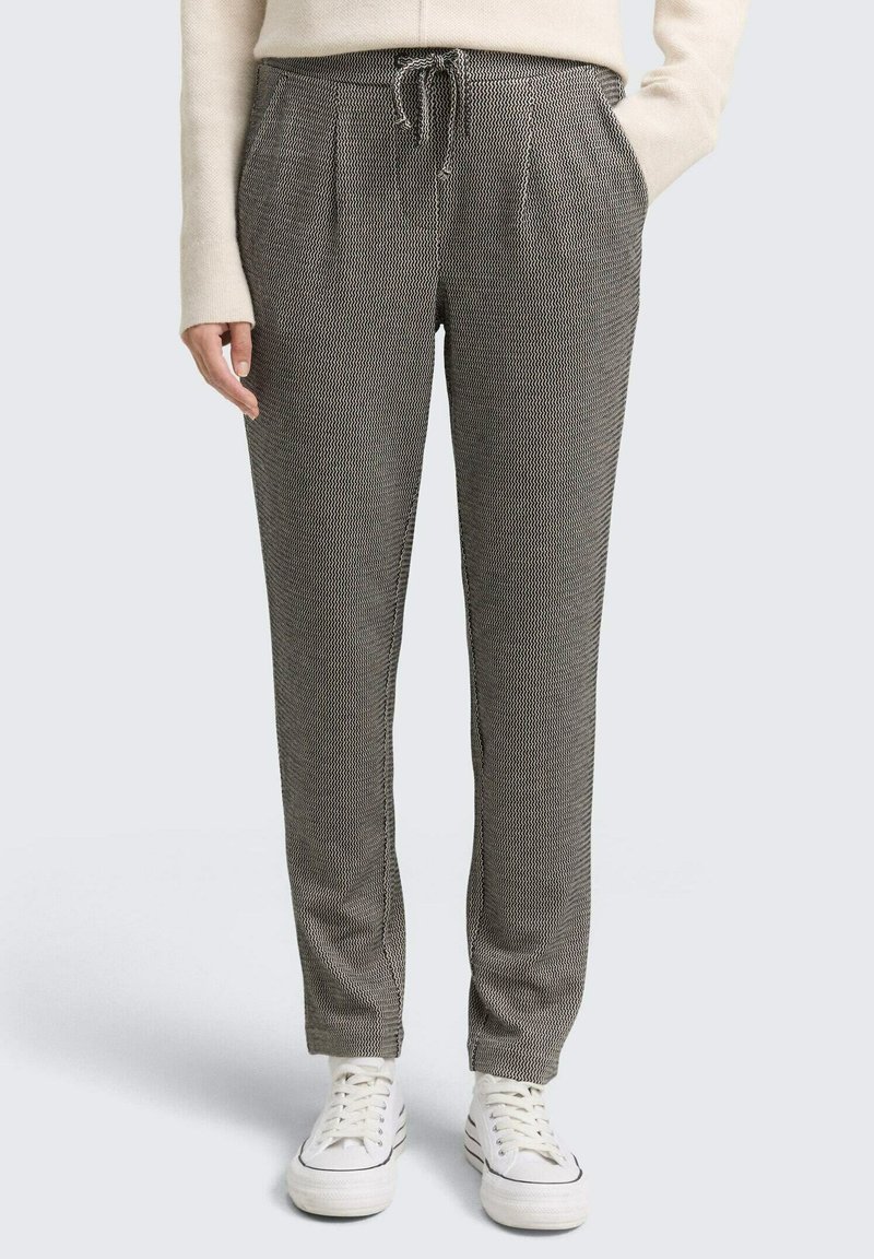 Grijze en zwarte geblokte broek met een elastische tailleband met trekkoord, zijzakken en taps toelopende pijpen, gecombineerd met witte sneakers.