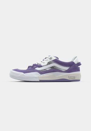 Baskets violettes et blanches avec un tissu texturé, présentant un profil bas, un système de laçage et un logo Vans au talon. Détails argentés sur le design.