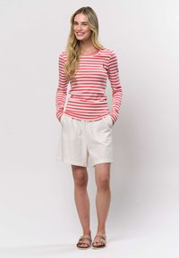 Punaste ja valgete triipudega pika varrukaga särk, erkrohelised püksid taskutega ning beežid sandaalid. Sile kangas ja kokkusobiv disain.