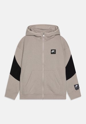Felpa con cappuccio grigio chiaro con cerniera, pannelli accentuati neri, due tasche frontali e patch con logo Nike Air sul petto e sulla manica. Tessuto dalla trama morbida.