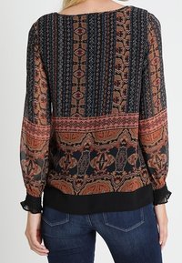 Blusa a maniche lunghe con motivo, caratterizzata da una base nera con accenti arancioni e bordeaux. Tessuto strutturato e polsini arricciati alle maniche.