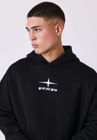 Zwarte hoodie van zacht materiaal met een kangoeroezak, met een wit geborduurd logo en sterontwerp aan de voorkant.