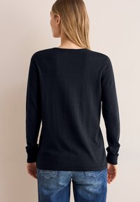 Mörkblå långärmad tröja i mjukt stickat material, med rundad halsringning och åtsittande ärmmuddar, tillsammans med blå denimjeans.