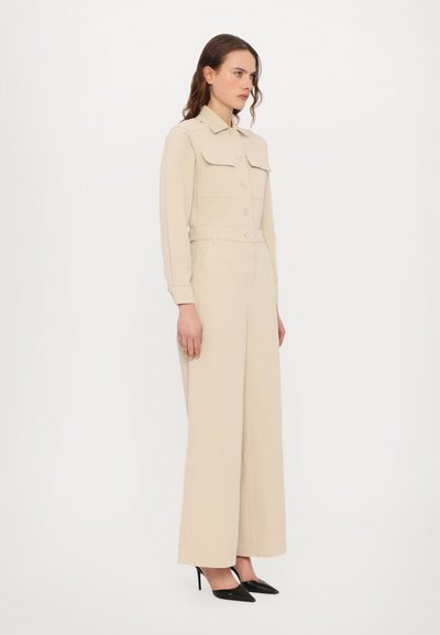 Beidzis jumpsuit ar garām piedurknēm, ar pogu aizdari priekšā, divām krūšu kabatām, jostu vestē un platu kāju dizainu. Nēsāts ar melniem smailiem papēžiem.