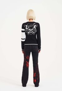 Black knitted sweater with white stripes and back skull graphic. Flared black jeans with red intricate pattern detailing along the sides.