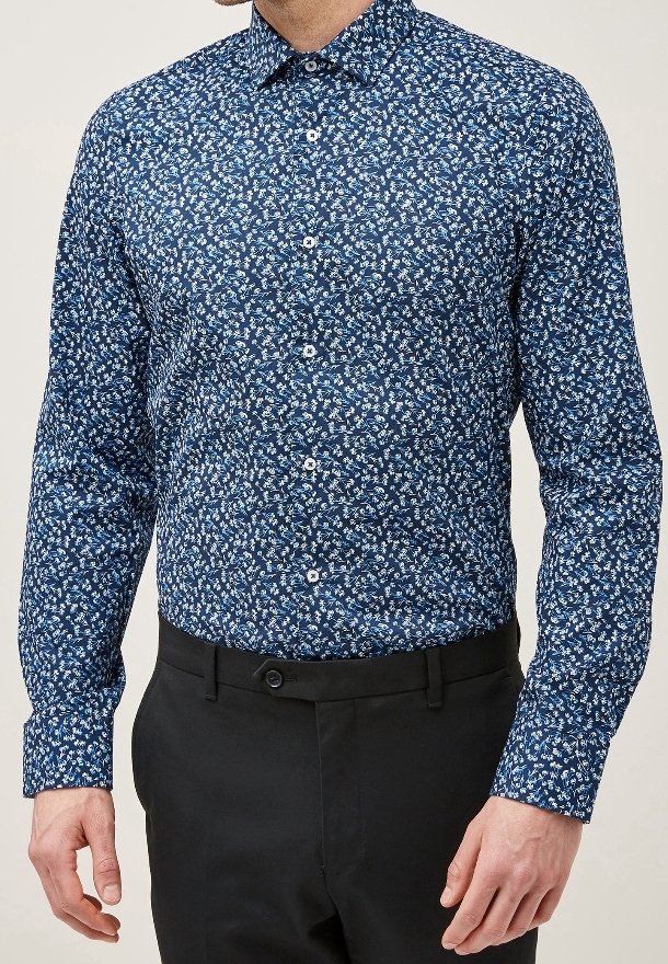 Homme portant une chemise bleue ajustée à manches longues avec des motifs floraux blancs, boutonnée à l'avant, associée à un pantalon noir.