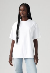 T-shirt blanc oversize en coton avec un col rond et des manches courtes. Assorti à un jean bleu clair à coupe décontractée.