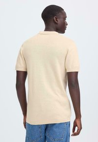 Polo beige à manches courtes présenté de dos, avec un col classique et une texture en maille légère et lisse.