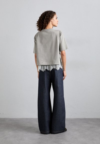 Γκρίζο κομμένο t-shirt με κοντά μανίκια, επικαλυμμένο με δαντέλα. Ζευγάρι παντελονιών από σκούρο τζιν με φαρδιά πόδια, ορατά ραφή και ακατέργαστο στρίφωμα.