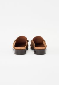 Back view of brown suede slip-on shoes, featuring an open back design, smooth leather insole, and a dark wooden block heel.