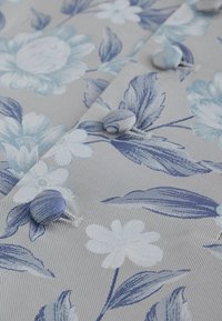 Bloemmotief stof in tinten blauw en wit op een grijze achtergrond. Bevat een gestructureerd oppervlak met knopen bekleed met stof.