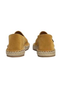 Zapatos amarillos de ante sin cordones con suela de yute trenzado y acabado suave, que presentan un respaldo redondeado y un diseño minimalista.