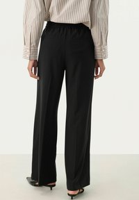 Pantalons larges noirs avec une taille élastique, dotés d'une texture lisse et de deux poches arrière, associés à une chemise à rayures à manches longues.