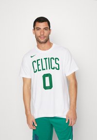Hvid bomulds t-shirt med "CELTICS" og nummer "0" i grønt, med Nike-logo på venstre skulder. Model iført grønne shorts.