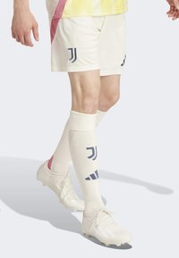 Valkoiset jalkapallosortsit, joissa on laivastonsininen logo, yhdistettyinä valkoisiin sukkiin, joissa on vaaleanpunaista ja laivastonsinistä yksityiskohtaa, sekä valkoisiin kengännauhoihin, joissa on kuviollinen pinta.