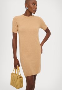 Knit short-sleeve dress in beige, featuring a round neckline and fitted silhouette. Paired with a yellow woven handbag.